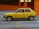 Żółty Audi 50, klasyk z lat 70., parkuje na tle pomarańczowej, kafelkowej architektury.