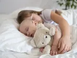 Dzieci śpią wtulone w misia. Starsza siostra czuwa nad maluszkiem, pokazując, ile śpi dwulatek i jak ważny jest sen dla rozwoju.