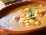 Una ciotola di terracotta piena di zuppa di fagioli cremosa, con pezzetti di carne e una fogliolina di menta. Perfetta per una cena confortante.