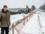 Mężczyzna wskazuje na plac budowy drogi. W tle koparka i pracownicy. Zima i specustawa drogowa utrudniają prace.