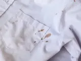 Biała koszula z licznymi brązowymi plamami z błota na kieszeni i rękawie.