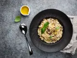 Kremowe risotto z grzybami na czarnym talerzu, obok łyżka i oliwa.