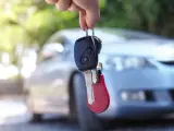 Kluczyki samochodowe z breloczkiem i symbolem immobilizera wiszą na palcu, na tle jasnego auta.