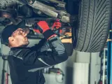 Mechanik w rękawicach dokręca sworzeń zwrotnicy w podwoziu samochodu.