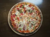 Cała pizza z różnymi dodatkami: salami, kukurydzą, papryczkami jalapeno, pieczarkami i ogórkiem.