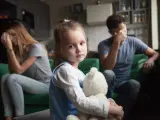 Smutna dziewczynka z misiem w objęciach, podczas gdy rodzice w tle przeżywają trudne chwile. Temat: rozwód a dzieci.