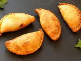 Cuatro empanadillas doradas y crujientes dispuestas sobre una superficie oscura, con hojas de menta a los lados.