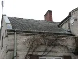Dach pokryty eternitem, który zawiera azbest. Co to za materiał? Stary, szary eternit na dachu domu, z kominem i anteną satelitarną.