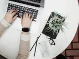 Kobieta pracuje na laptopie, obok leżą okulary, telefon i roślina. To idealne zdjęcia w chmurze do inspiracji.