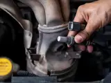 Druga sonda lambda objawy: mechanik trzyma nową sondę lambda przy kolektorze wydechowym.