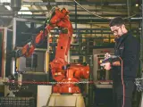 Un tecnico controlla un braccio robotico rosso in una fabbrica, dimostrando la meccatronica cos'è: l'integrazione di meccanica, elettronica e informatica.
