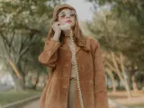 Kobieta w brązowej zamszowej kurtce damskiej rozmawia przez telefon w stylu retro.