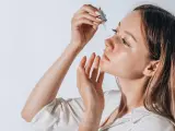 Frauenhand trägt Tropfen eines Serums auf ihr Gesicht auf. Ob Squalan oder Hyaluron, die Haut strahlt Feuchtigkeit aus.