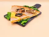 Kawałek pysznej pizzy capriciosa z szynką, serem i pieczarkami na ciemnej desce, ozdobiony rukolą.