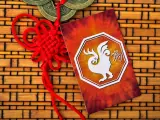 Czerwony sznur szczęścia i karta z białym kogutem, symbolem chińskiego zodiaku, na tle bambusowej maty.