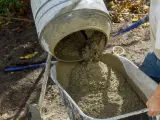 Betoniarka wylewa świeży beton do taczki. Właściwa ilość cementu na 1 m3 betonu jest kluczowa dla jego wytrzymałości.
