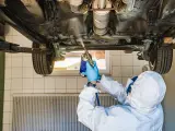 Mechanik w kombinezonie zabezpieczającym podwozie samochodu. Zastanawiasz się, ile kosztuje przegląd samochodu z gazem?