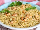 Un plato de espaguetis con gambas, adornado con hojas de albahaca fresca y perejil picado.