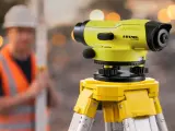 Żółty niwelator precyzyjnie mierzy poziomy na budowie. To narzędzie geodezyjne, które pomaga w pracach ziemnych.