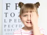 Dziewczynka zasłaniająca oko ręką na tle tablicy Snellena.
