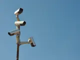 Cztery kamery monitoringu na słupie, czujne oko inwigilacji wpatrujące się w błękitne niebo.