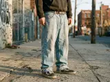 Ragazzo con baggy jeans uomo outfit, felpa scura e sneakers Vans, in un vicolo urbano con graffiti.