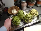 Quatre artichauts verts prêts pour la cuisson vapeur. Une main tient le plateau.