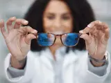 Okulary relaksacyjne wady wzroku? Kobieta w białym kitlu prezentuje okulary z niebieskimi soczewkami, które odbijają wnętrze sklepu.