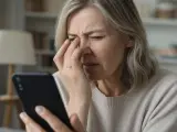 Donna anziana con disturbi visivi, forse cerchi luminosi, si tocca gli occhi mentre guarda uno smartphone.