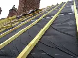 Charpente de toiture avec isolant noir et liteaux en bois, près de cheminées en brique.