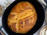 Ein goldbraunes Brot mit knuspriger Kruste liegt in einem Gusseisentopf. Dieses Brot kommt nicht aus dem Topf, sondern wurde darin gebacken.