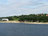 Słoneczny dzień nad jeziorem Chańcza. Piękna plaża, las i kilka domków w tle. Ludzie odpoczywają i kąpią się.