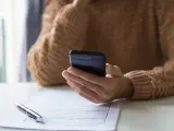 Persona revisa su teléfono móvil, modelo 035, mientras tiene un bolígrafo y un formulario de solicitud sobre la mesa.