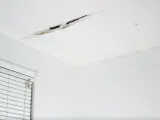 Widoczne pęknięcia na suficie w starym domu, świadczące o jego wieku i potrzebie remontu.