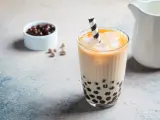 Erfrischendes Bubble Eis mit Tapiokaperlen und Eiswürfeln in einem Glas, daneben eine Schale mit dunklen Perlen.