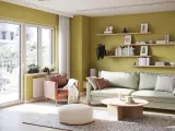 Jasnozielone kolory ścian inspiracje: przytulny salon z pastelową sofą, ceglastym fotelem i drewnianymi półkami pełnymi książek.