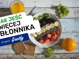 Pyszna owsianka z owocami i nasionami chia, idealna na śniadanie, które ma duzo blonnika. Obok szklanka soku i kromki chleba.