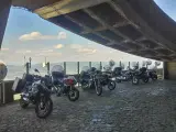 Motocykle pod betonowym zadaszeniem, z widokiem na krajobraz przypominający szwajcarskie Czechy.