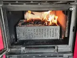 Estufa de pellets ardiendo dentro de un hueco de chimenea. El combustible se quema en una bandeja metálica perforada.