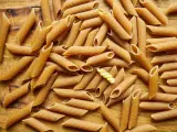 Mnóstwo makaronu pełnoziarnistego penne na drewnianym blacie. Idealny wybór dla dbających o linię, bo makaron pełnoziarnisty kcal ma mniej!