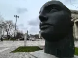 Duża, ciemna rzeźba głowy Igora Mitoraja na tle Teatru Dramatycznego w Warszawie.