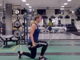 Kvinna utför utfallssteg med vikt i ett gym. Hon håller en hantel i ena handen och har ett ben framåt och ett bakåt.