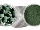 Dwie szklane miseczki: jedna z tabletkami chlorelli, druga z zielonym proszkiem. Dowiedz się, chlorella jak stosować, by czerpać z niej korzyści.