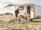 Ett par njuter av en stranddag med sina tyska husvagnar. Solen skiner och sanddynerna skapar en vacker bakgrund.