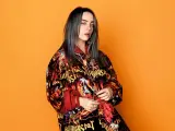 Billie Eilish teraz w kolorowej kurtce z nadrukiem na pomarańczowym tle.