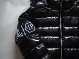 Błyszcząca, czarna kurtka Philipp Plein z futrzanym kapturem i białym logo na rękawie.