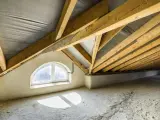 Poddasze w trakcie budowy, widoczne drewniane krokwie o kącie nachylenia dachu 30 stopni, okno łukowe i betonowa podłoga.