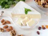 Queso brie en cuña y trozos, decorado con menta. Alrededor hay almendras, nueces y frutos secos. Ideal para quienes buscan información sobre queso brie calorias.