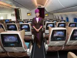 Uśmiechnięta stewardessa Etihad Airways w brązowym mundurku stoi w rzędzie foteli. Ekraniki pokazują astronautę. Dobre etihad airways opinie.