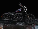 Czarny Harley-Davidson Iron 1200 z kolorowym paskiem na baku, stojący na mokrej, błyszczącej nawierzchni.